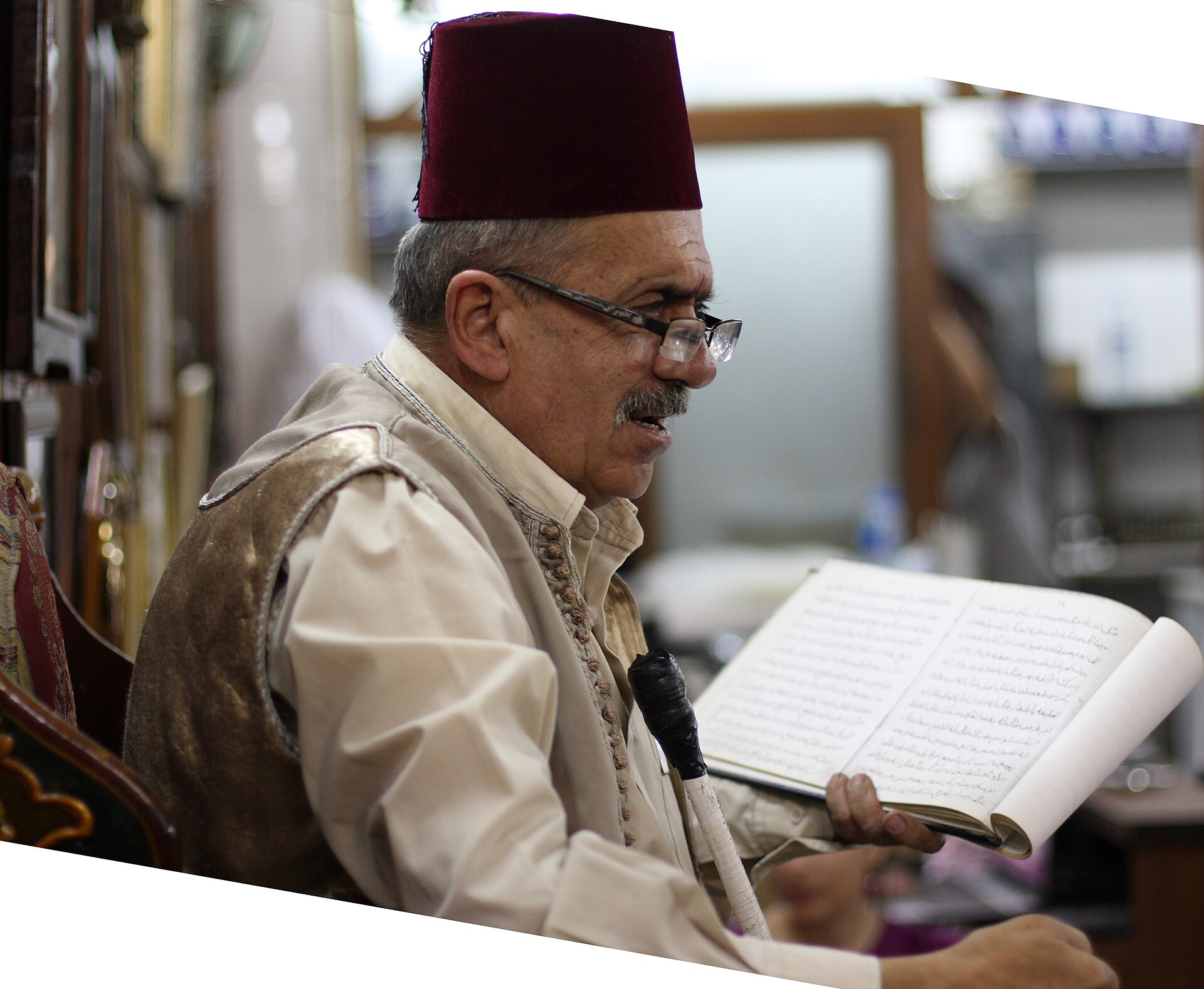 حكواتي بطربوش يقرأ بصوت عالٍ من كتاب في مقهى دمشقي.